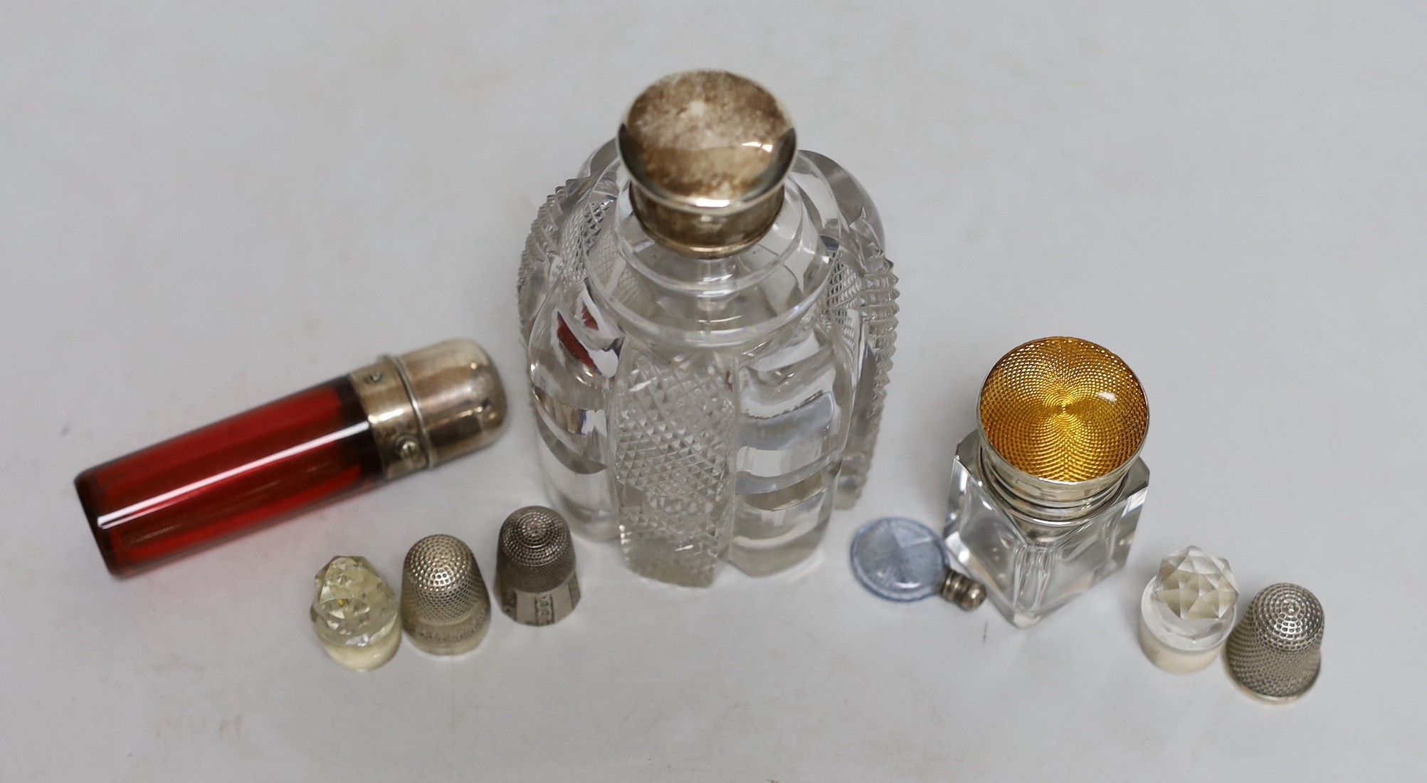 Three silver or white metal mounted glass scent bottles including enamelled, 56mm and ruby glass, one other, two glass stoppers and three thimbles.